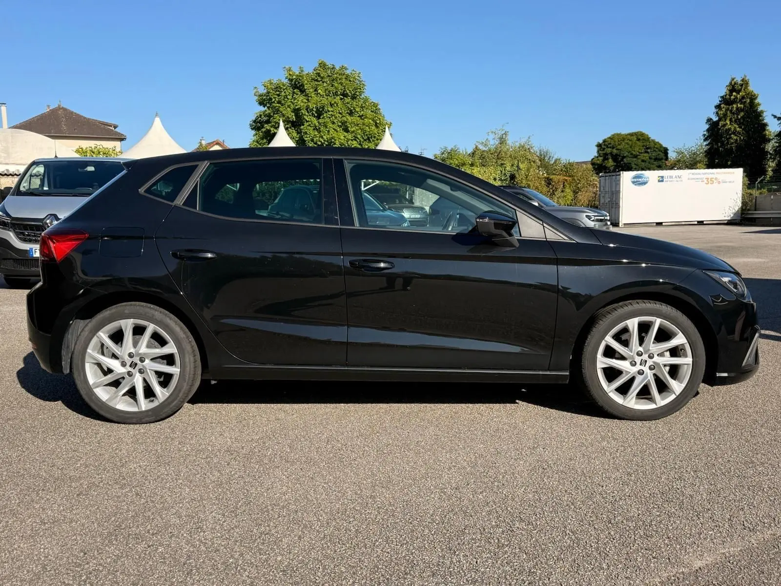 Profil droit d'une SEAT Ibiza 1.0 TSI 95 FR noire garée sur un sol goudronné sous un ciel bleu clair.