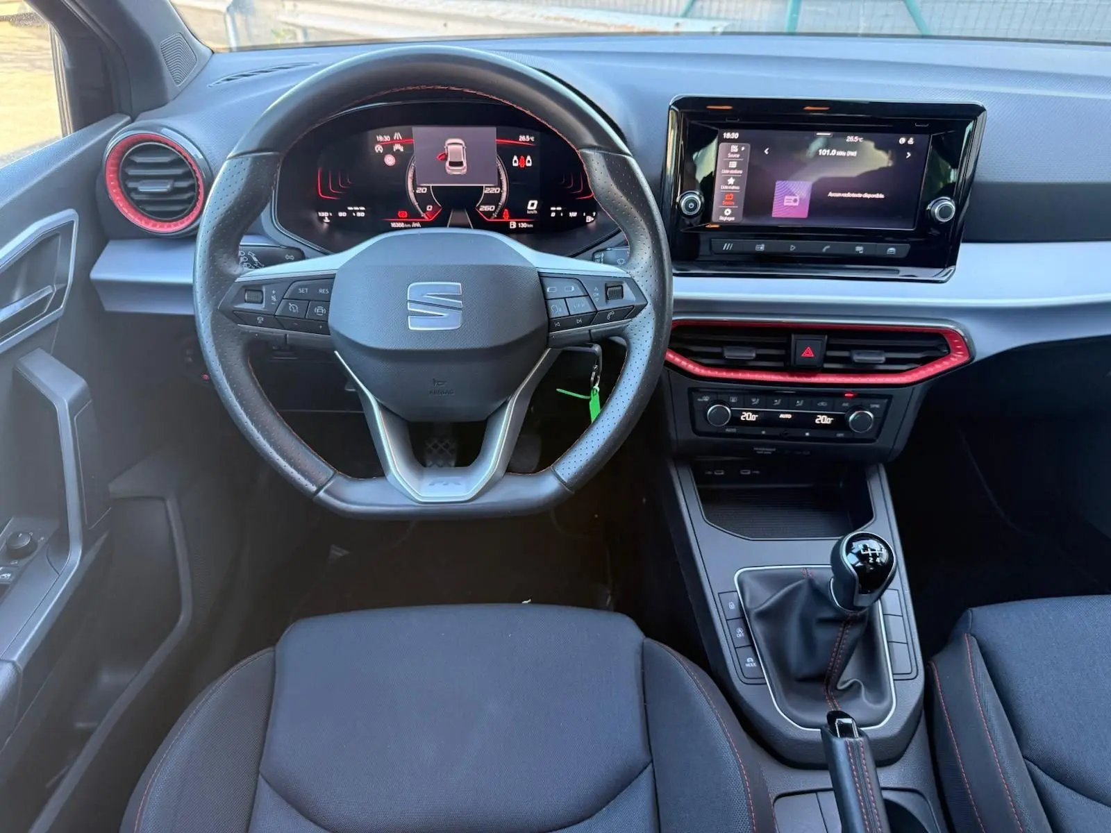 Vue intérieure frontale du tableau de bord et volant noir de la SEAT Ibiza 1.0 TSI 95 FR avec détails rouges et écran tactile.