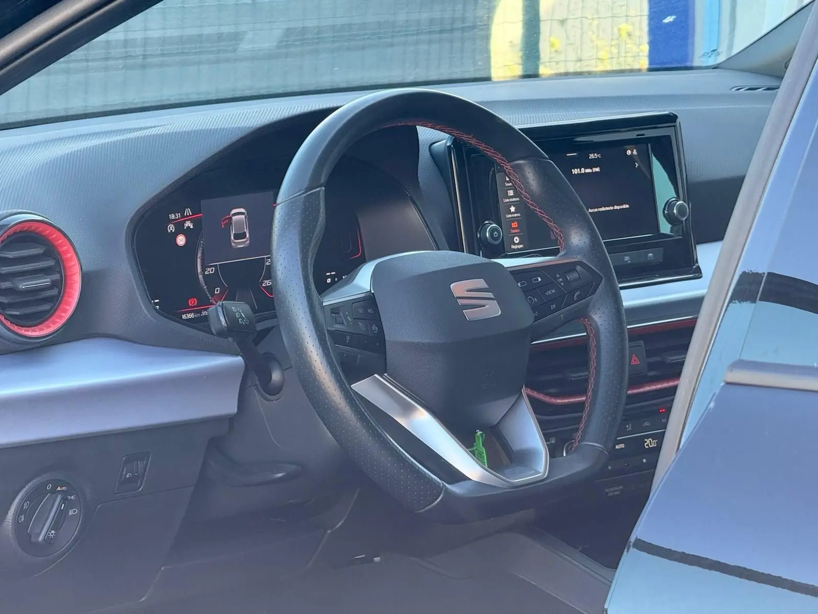 Vue intérieure du poste de conduite d'une SEAT Ibiza noire, volant cuir avec surpiqûres rouges et écran tactile central.