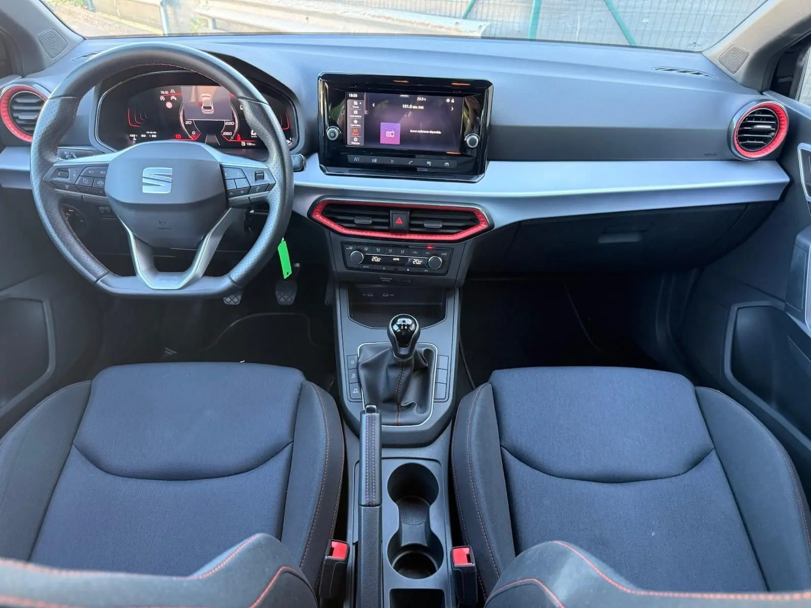 Vue intérieure avant de la SEAT Ibiza 1.0 TSI 95 FR 2025 avec volant cuir, écran tactile central et détails rouges sur les aérateurs.