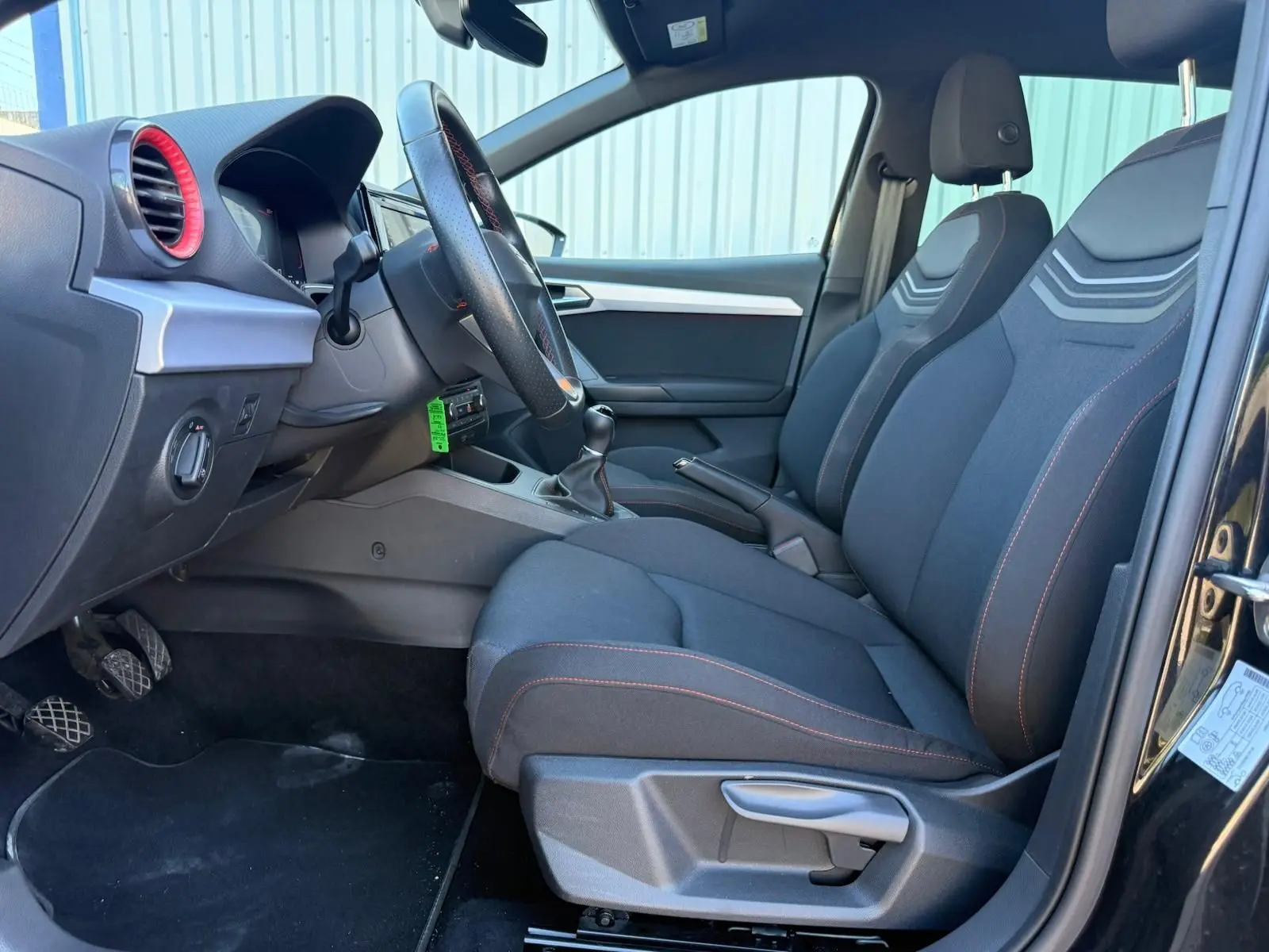 Vue intérieure côté conducteur de la SEAT Ibiza 1.0 TSI 95 FR noire, sièges tissu avec surpiqûres rouges et volant cuir.