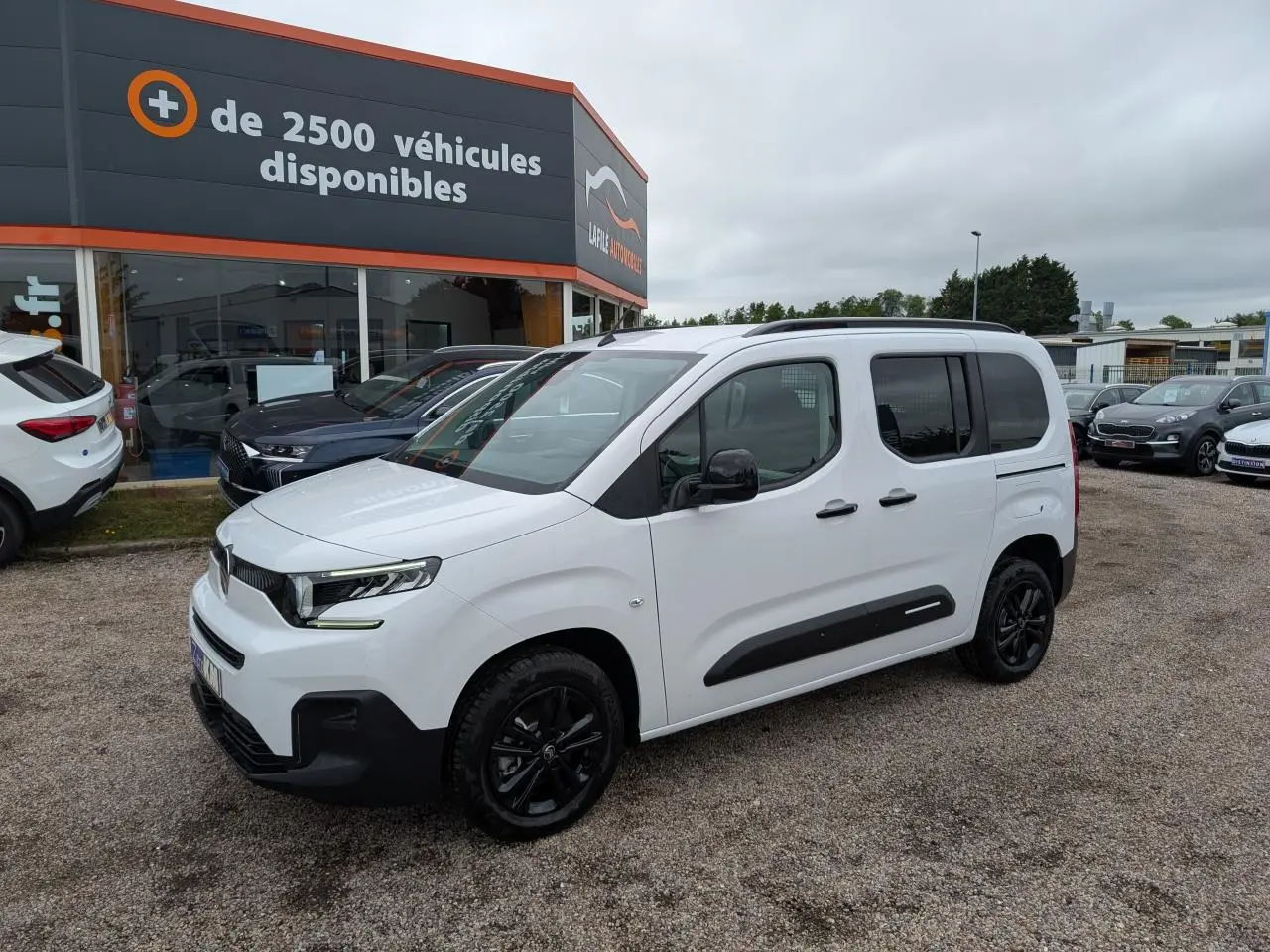 Citroën Berlingo blanc en 3/4 avant droit avec barres de toit noires et jantes alliage noires.