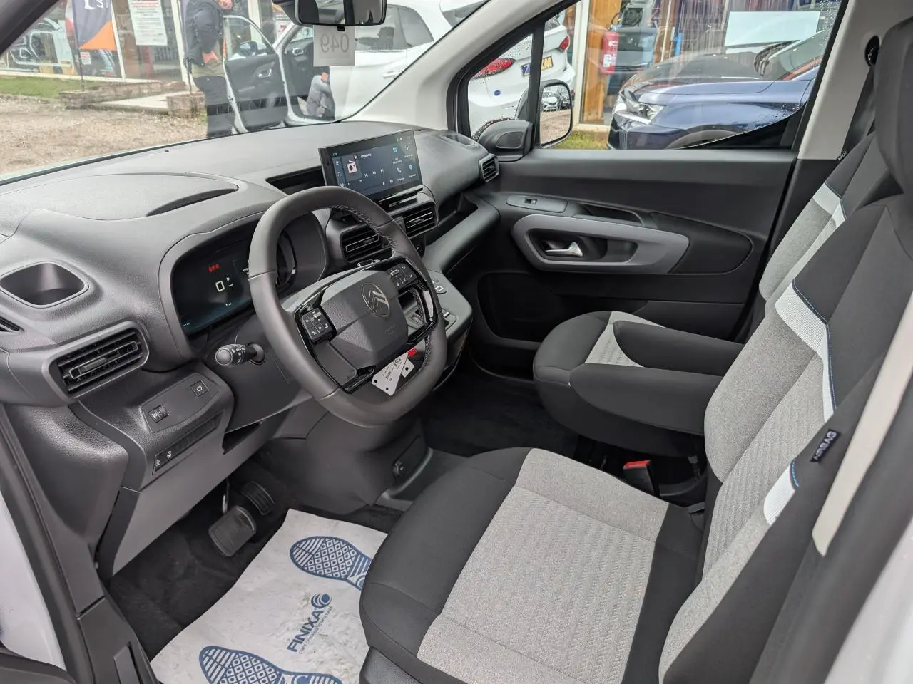 Vue intérieure côté conducteur du Citroën Berlingo blanc 2025, volant cuir multifonctions et sièges tissu bicolores.