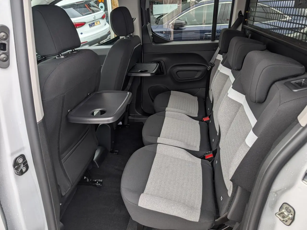 Vue intérieure côté droit sur les trois sièges arrière gris et noir avec tablette rabattable du Citroën Berlingo blanc.