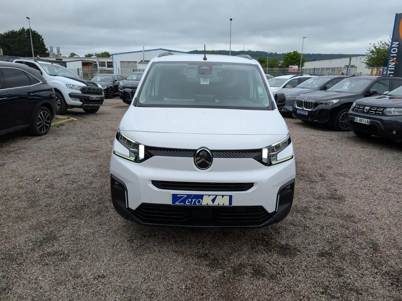 Vue de face du Citroën Berlingo blanc avec calandre noire et phares LED allumés sur un parking.