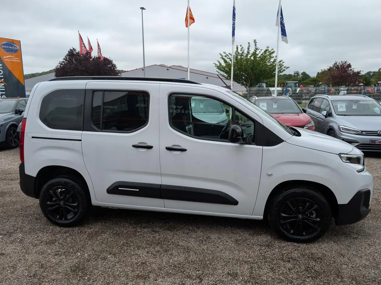 Vue de profil côté gauche d'un Citroën Berlingo blanc avec barres de toit noires et jantes alliage noires.