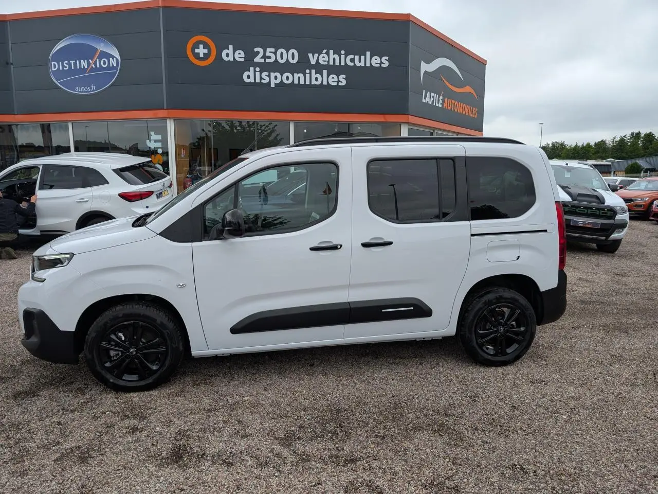 Vue de profil côté gauche d'un Citroën Berlingo blanc avec barres de toit noires et jantes alliage noires.