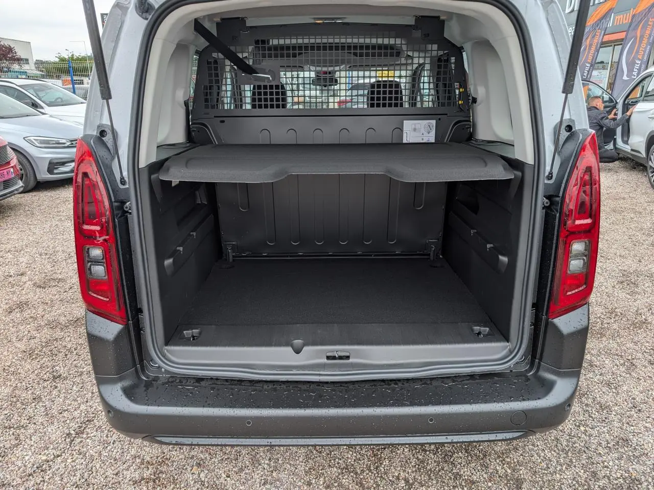 Vue arrière du coffre ouvert du Citroën Berlingo blanc 2025 avec séparation grillagée et tablette de rangement.