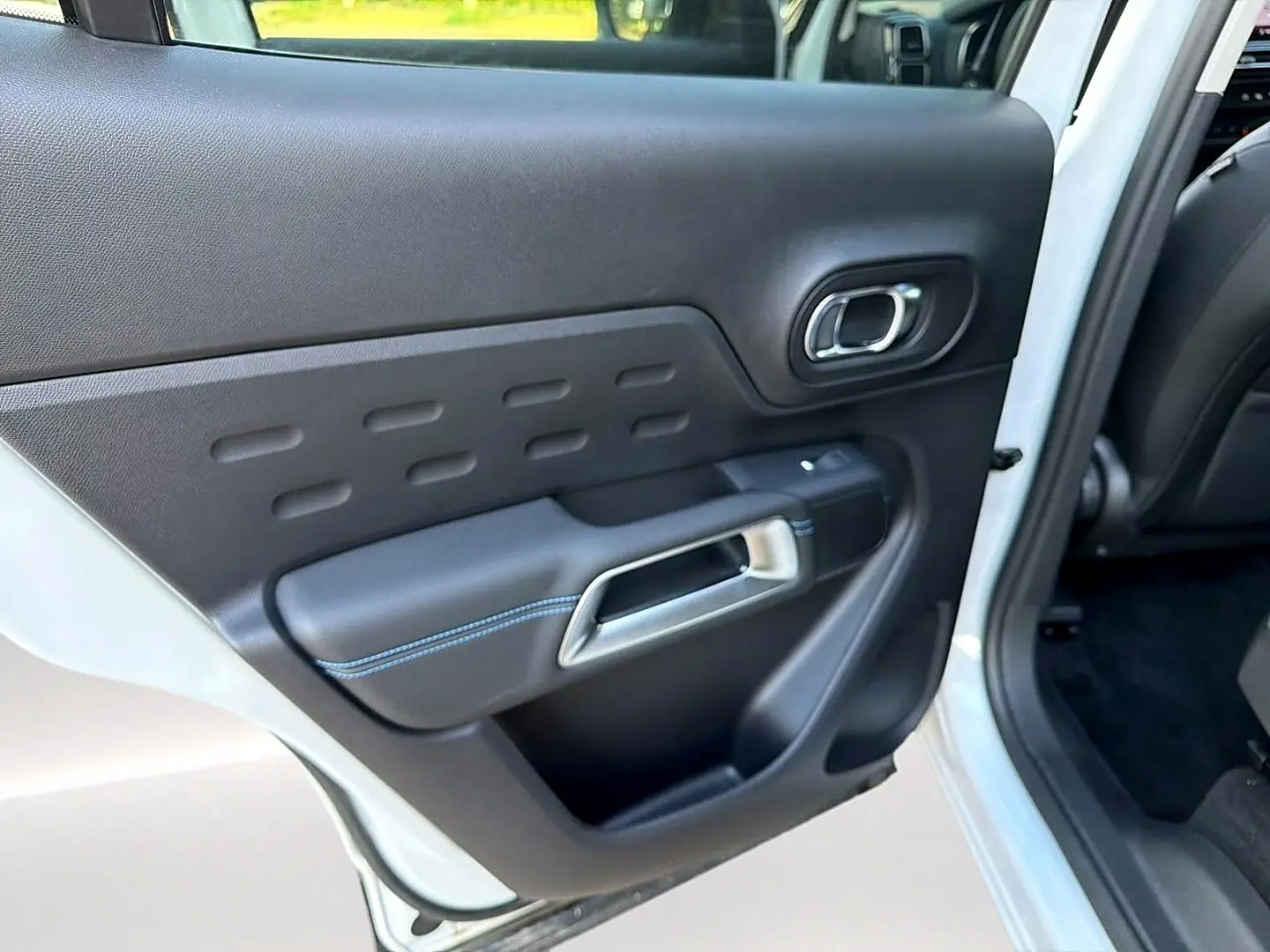 Vue intérieure côté gauche de la porte arrière blanche du Citroën C5 Aircross avec poignée argent et surpiqûres bleues.