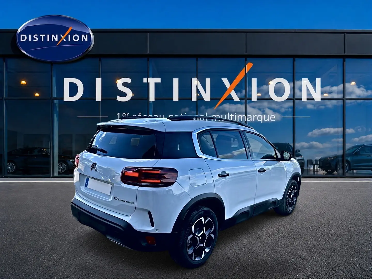 Vue 3/4 arrière droite d'un Citroën C5 Aircross blanc avec jantes alu et vitres arrière teintées devant une vitrine Distinxion.