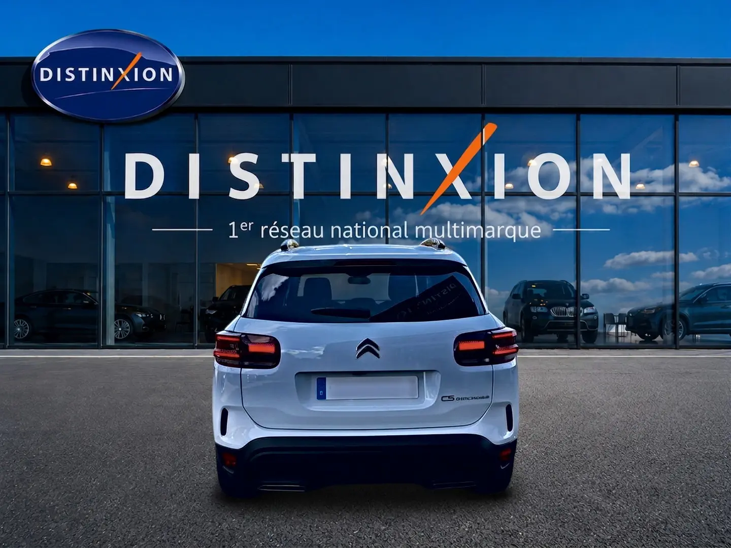 Vue arrière d'un Citroën C5 Aircross blanc 2025, avec feux LED et barres de toit visibles devant une vitrine Distinxion.