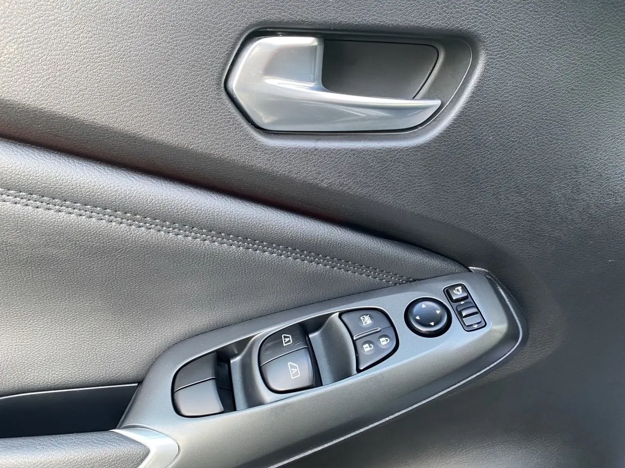 Détail de la porte intérieure côté conducteur du Nissan Juke 2025 en tissu noir avec commandes des vitres et poignée argentée.