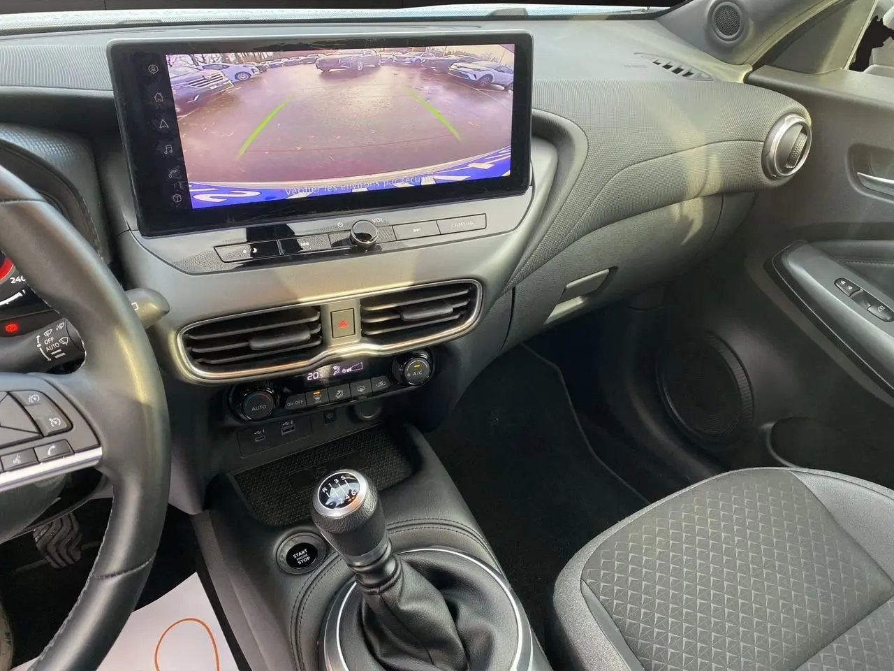 Vue intérieure côté passager du tableau de bord et console centrale du Nissan Juke 2025, avec écran tactile et sellerie tissu noir.