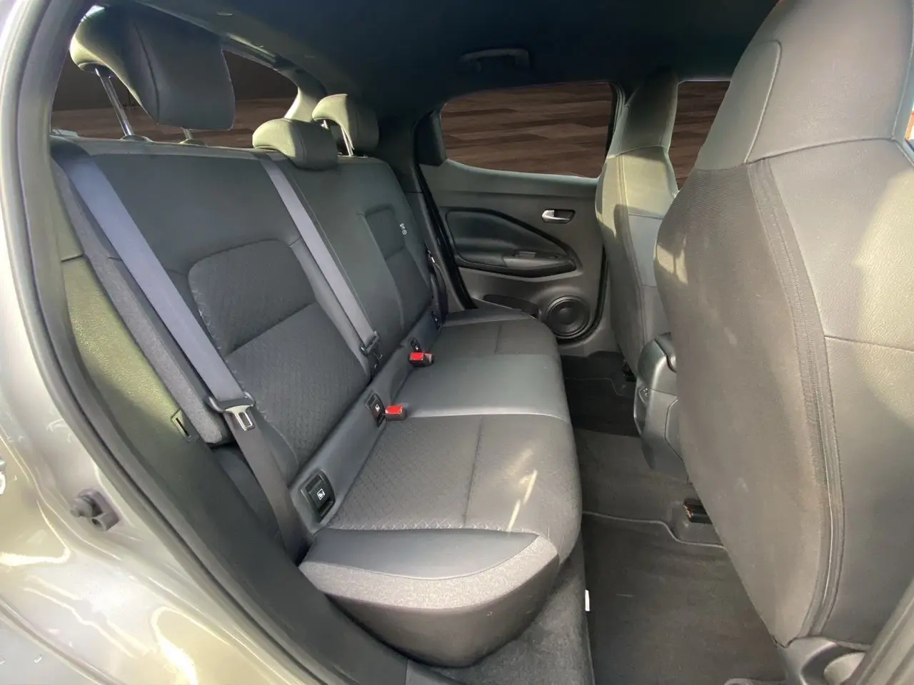 Vue intérieure arrière côté droit du Nissan Juke 2025 gris perle, montrant la banquette tissu noir et les ceintures de sécurité.