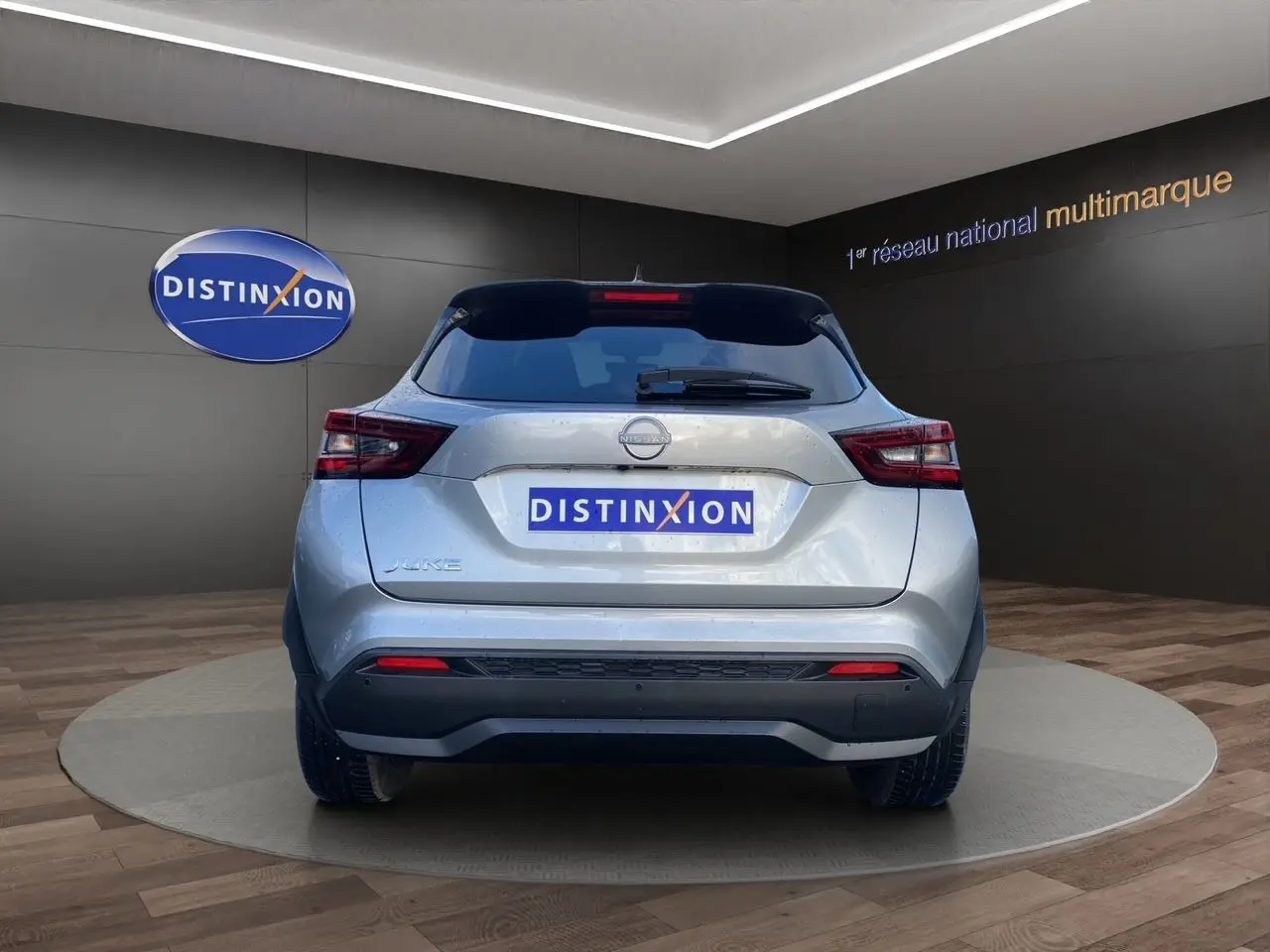 Vue arrière d'un Nissan Juke 2025 gris perle avec toit noir et feux LED, sur fond showroom Distinxion.
