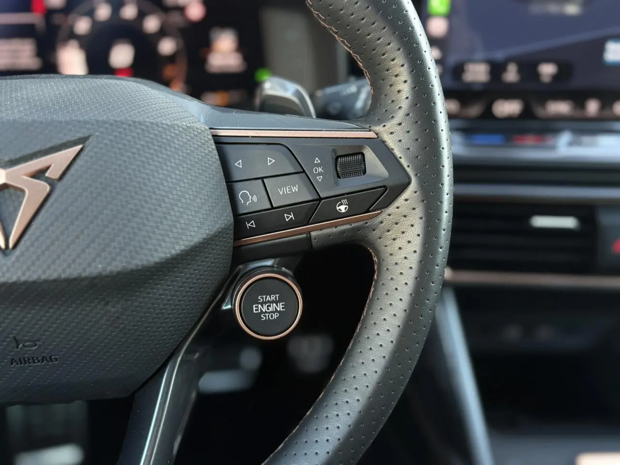 Gros plan sur le volant cuir perforé de la CUPRA Leon blanc Neige avec boutons multifonctions et bouton Start Engine Stop.