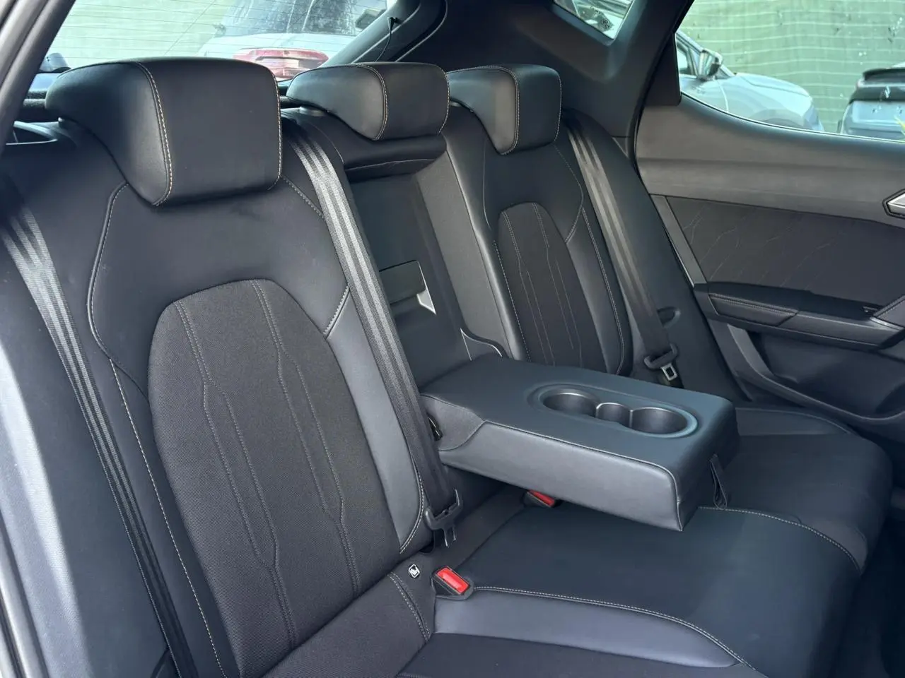 Vue intérieure des sièges arrière noirs bimatière avec accoudoir central rabattable et porte-gobelets de la CUPRA Leon 2025.