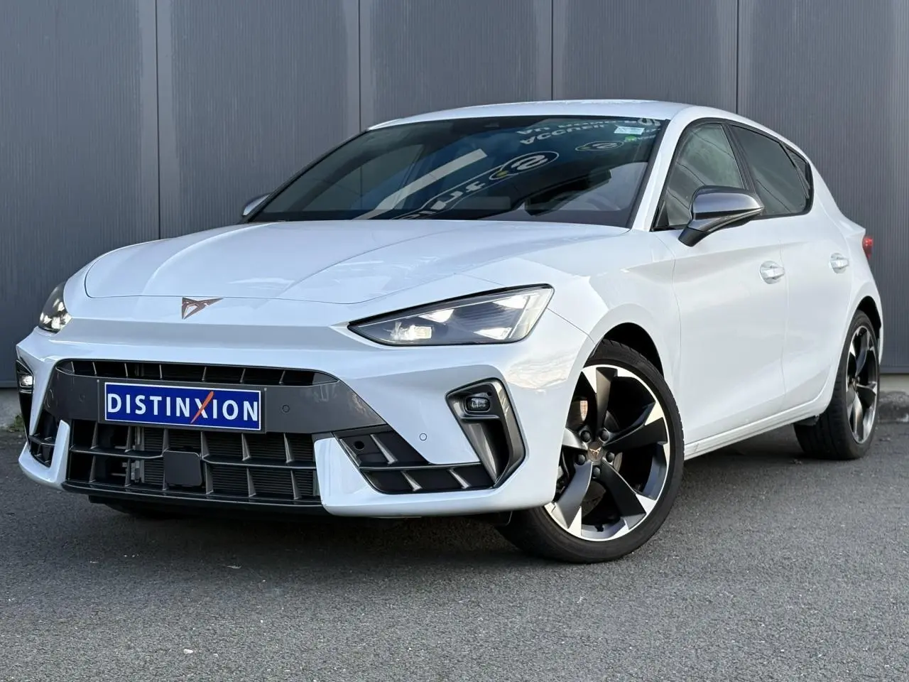 Vue 3/4 avant droite d'une CUPRA Leon blanche Neige avec jantes alliage noires et grises, calandre et phares LED distinctifs.