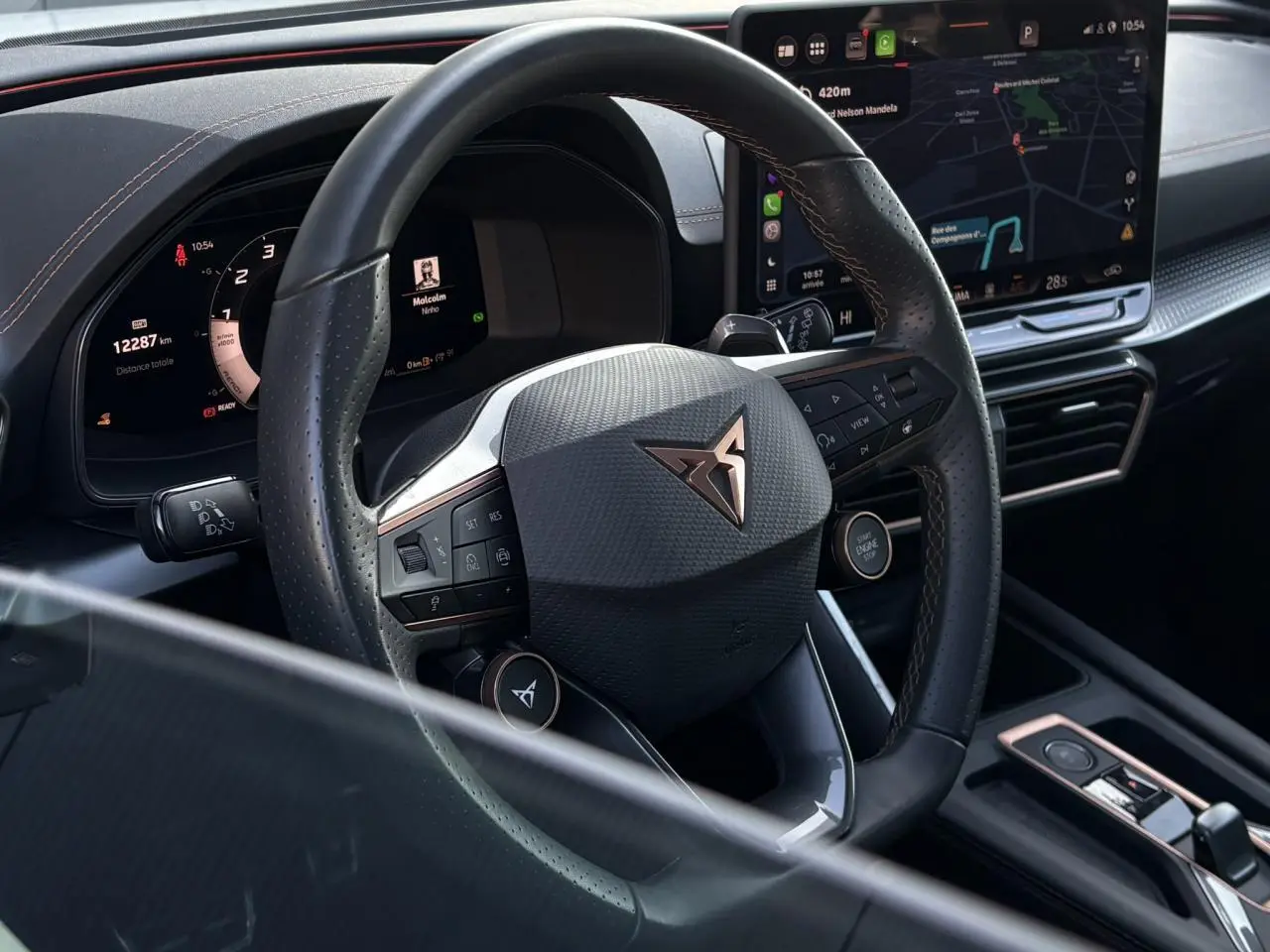 Vue rapprochée du volant noir perforé de la CUPRA Leon 2025 avec logo cuivre et tableau de bord digital.