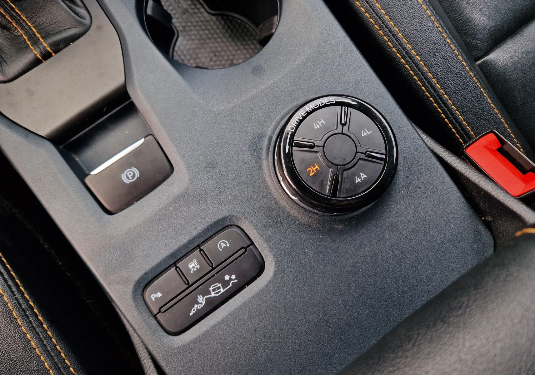 Gros plan sur la console centrale noire du Ford Ranger Wildtrak 2023, avec molette de modes de conduite et coutures orange.
