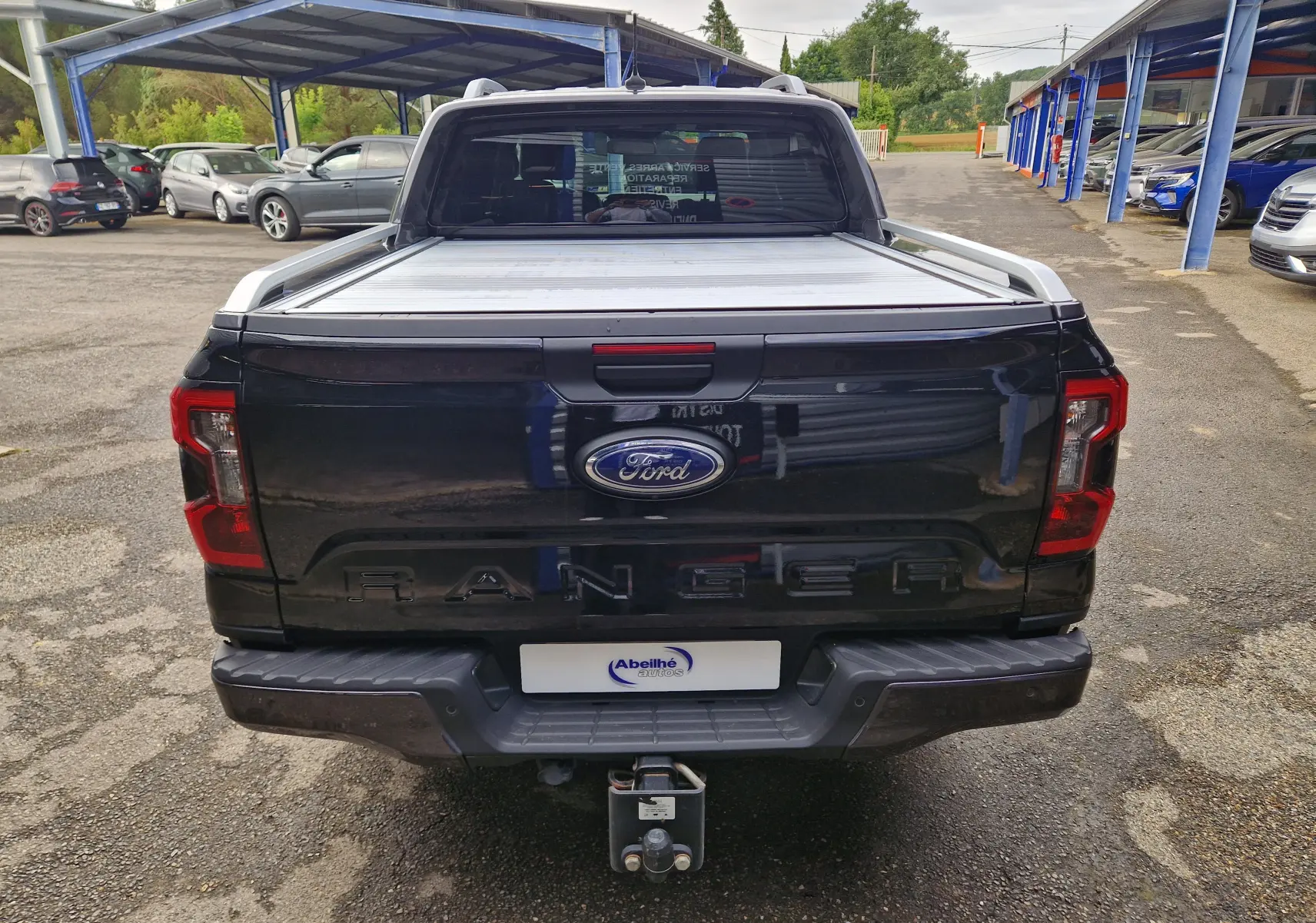 Vue arrière d'un Ford Ranger Wildtrak noir 2023 avec rideau de plateau coulissant et attelage visible.