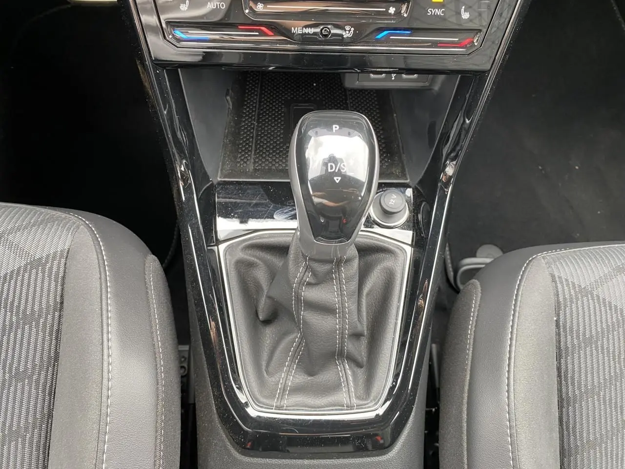 Vue rapprochée de la console centrale du Volkswagen T-Cross gris, mettant en valeur le levier de vitesse DSG7 et les sièges tissu noirs.