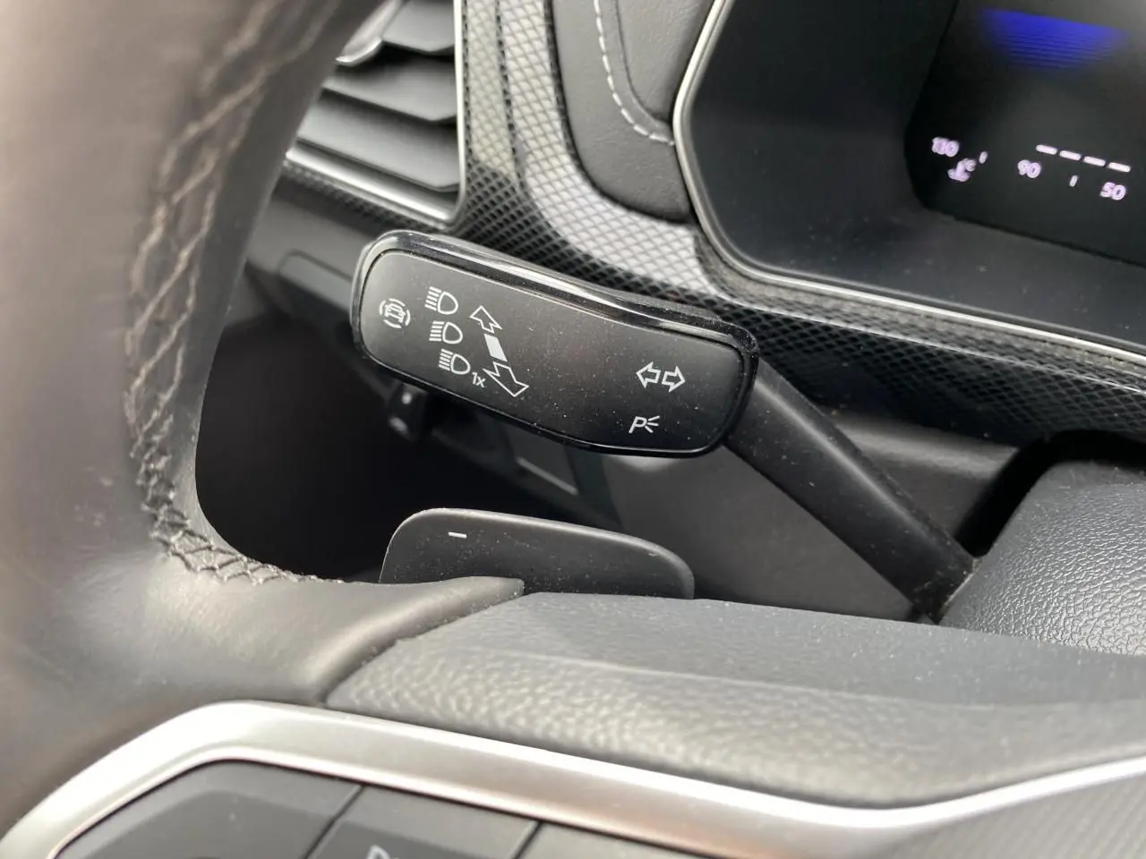 Gros plan sur la manette de clignotant noire du Volkswagen T-Cross 2024, avec volant cuir et tableau de bord gris.