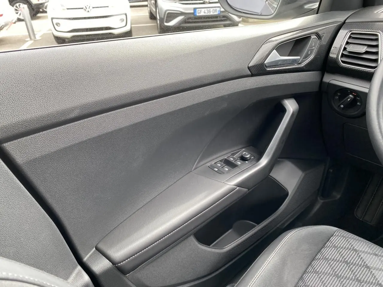 Vue intérieure côté gauche de la porte avant grise du Volkswagen T-Cross 2024 avec commandes de vitres et rétroviseurs.