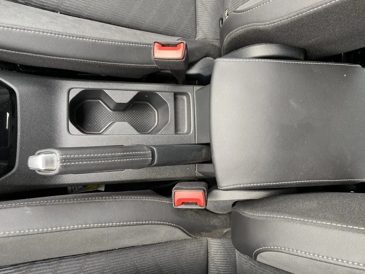 Vue plongeante sur la console centrale noire du Volkswagen T-Cross 2024 avec frein à main manuel et porte-gobelets.