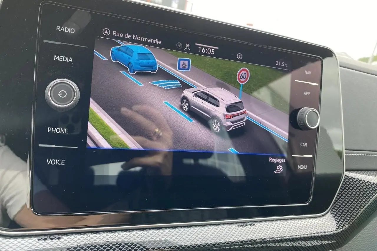 Écran tactile intérieur montrant l’assistance de conduite du Volkswagen T-Cross gris en vue 3/4 arrière sur route.