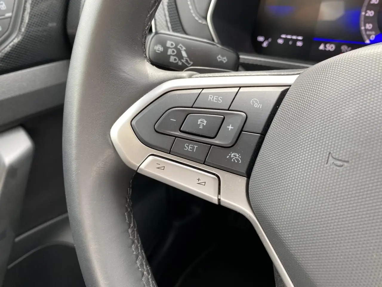 Gros plan sur le volant cuir gris du Volkswagen T-Cross 2024, avec commandes multifonctions et affichage digital en arrière-plan.