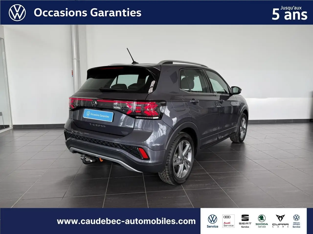 Volkswagen T-Cross gris en 3/4 arrière droit, avec attelage amovible, dans un showroom lumineux.