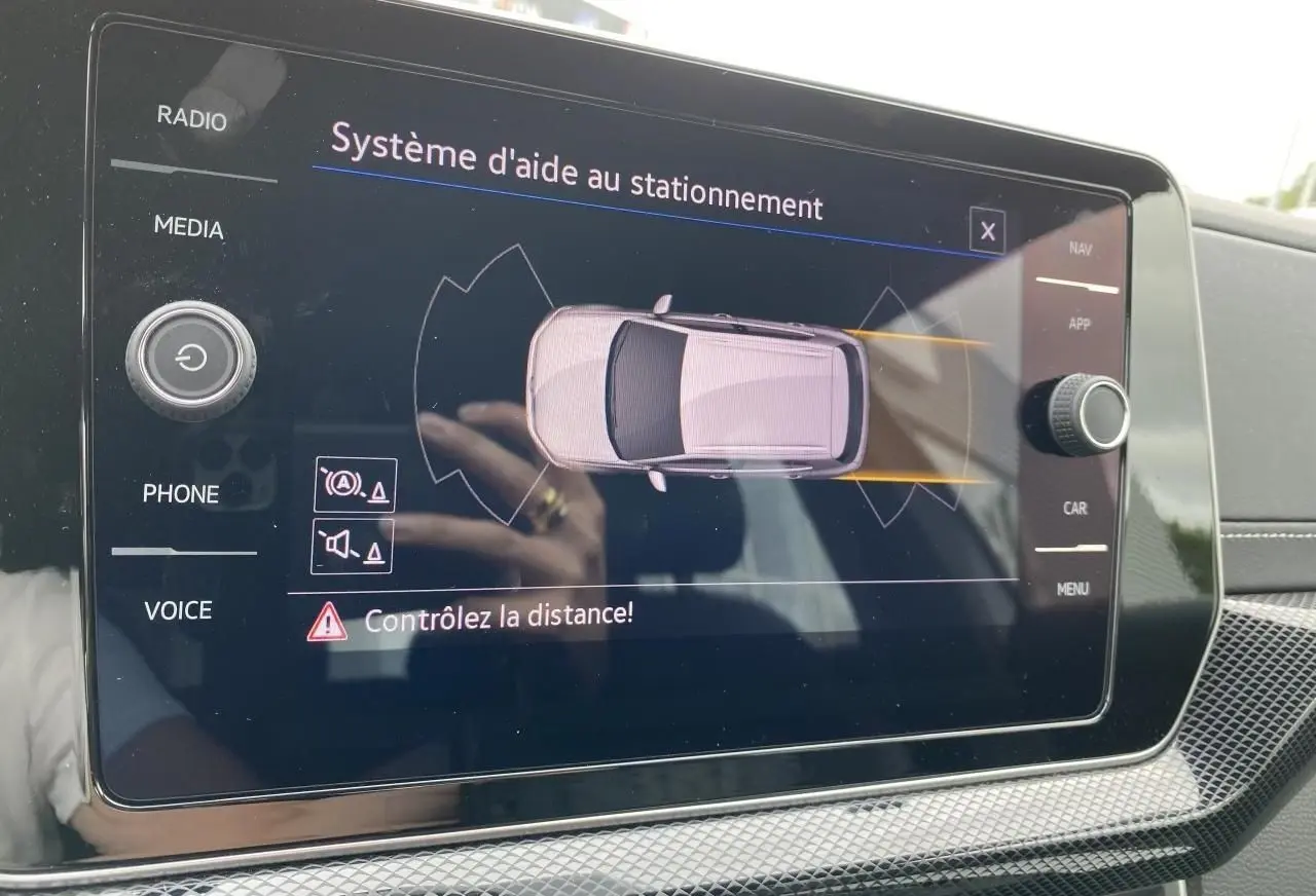 Écran tactile du système d'aide au stationnement montrant un Volkswagen T-Cross gris vu de dessus.