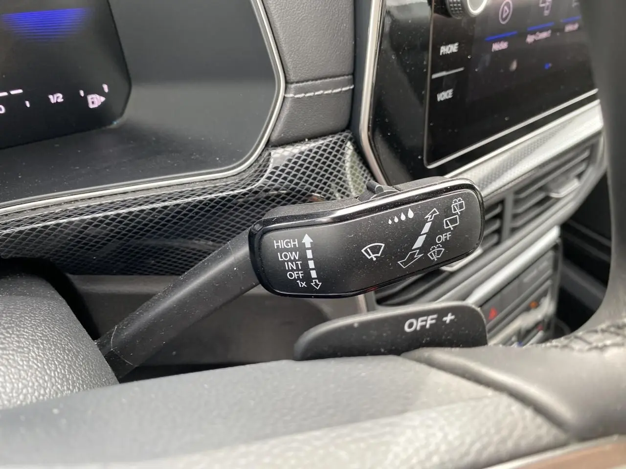 Gros plan sur la commande d’essuie-glace du Volkswagen T-Cross gris 2024, avec tableau de bord et écran tactile en arrière-plan.