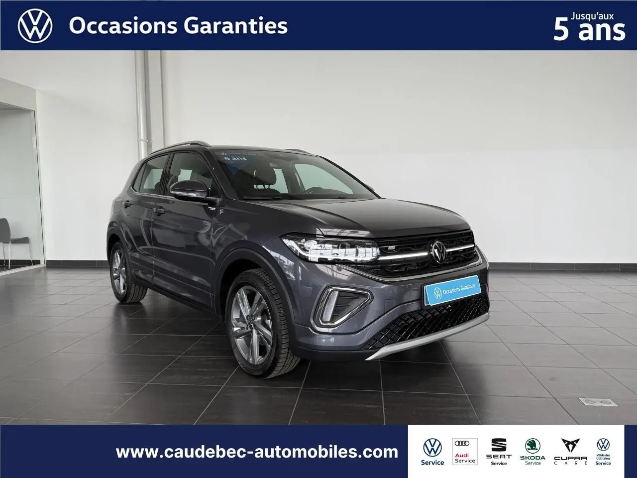 Volkswagen T-Cross gris en 3/4 avant droit, avec calandre noire et jantes alliage visibles en showroom.