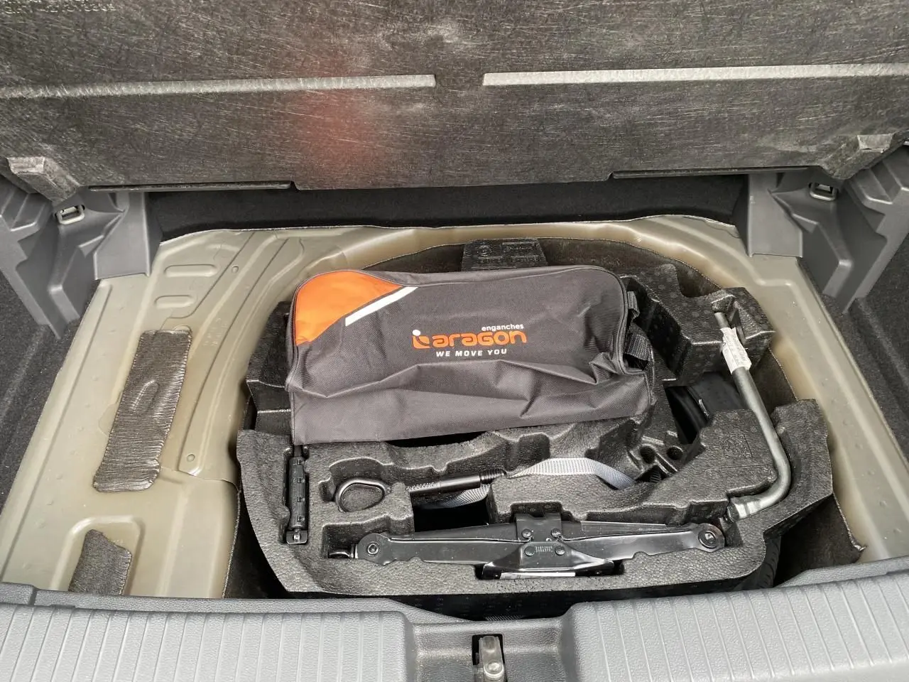 Vue plongeante sur la roue de secours et l’outillage de bord dans le coffre du Volkswagen T-Cross gris 2024.
