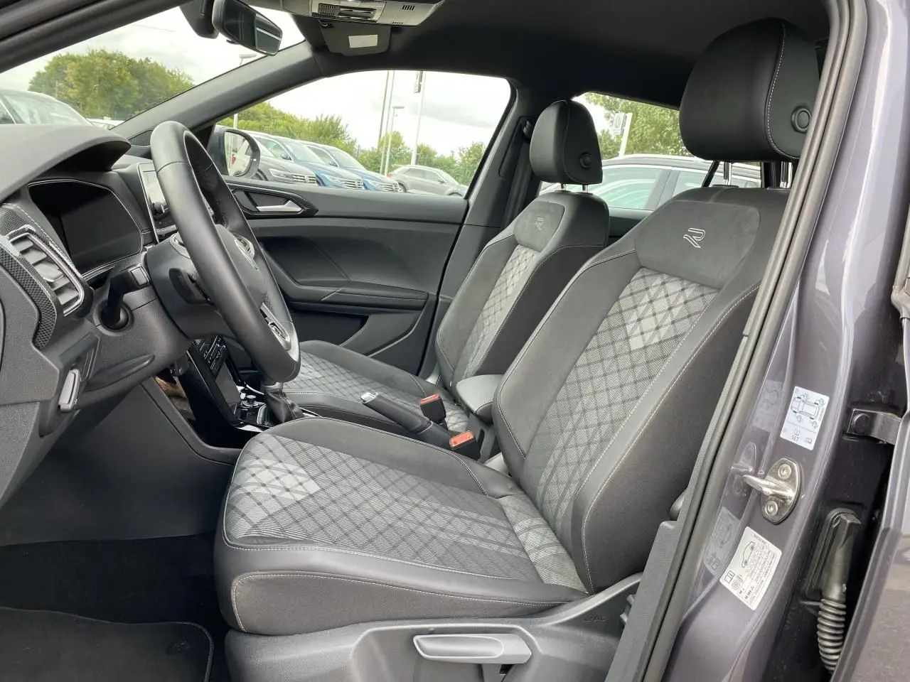 Vue intérieure côté conducteur du Volkswagen T-Cross gris 2024, sièges avant avec surpiqûres et logo R brodé.