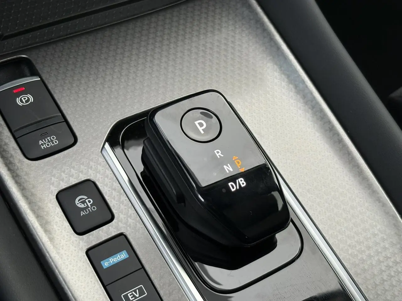 Gros plan sur la commande de boîte automatique noire avec boutons e-Pedal et frein à main électrique du Nissan Qashqai gris Ceramic.