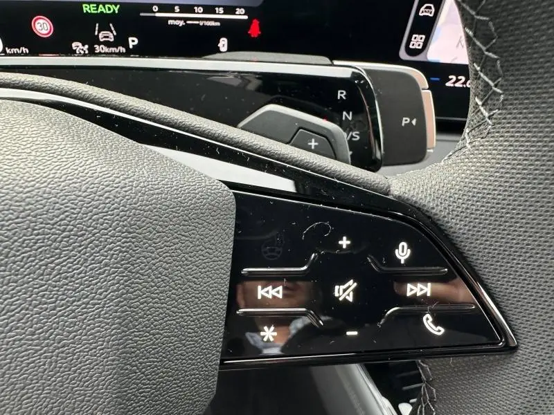 Gros plan sur les commandes au volant cuir noir de l’Audi Q3 2026, avec affichage numérique du tableau de bord en arrière-plan.