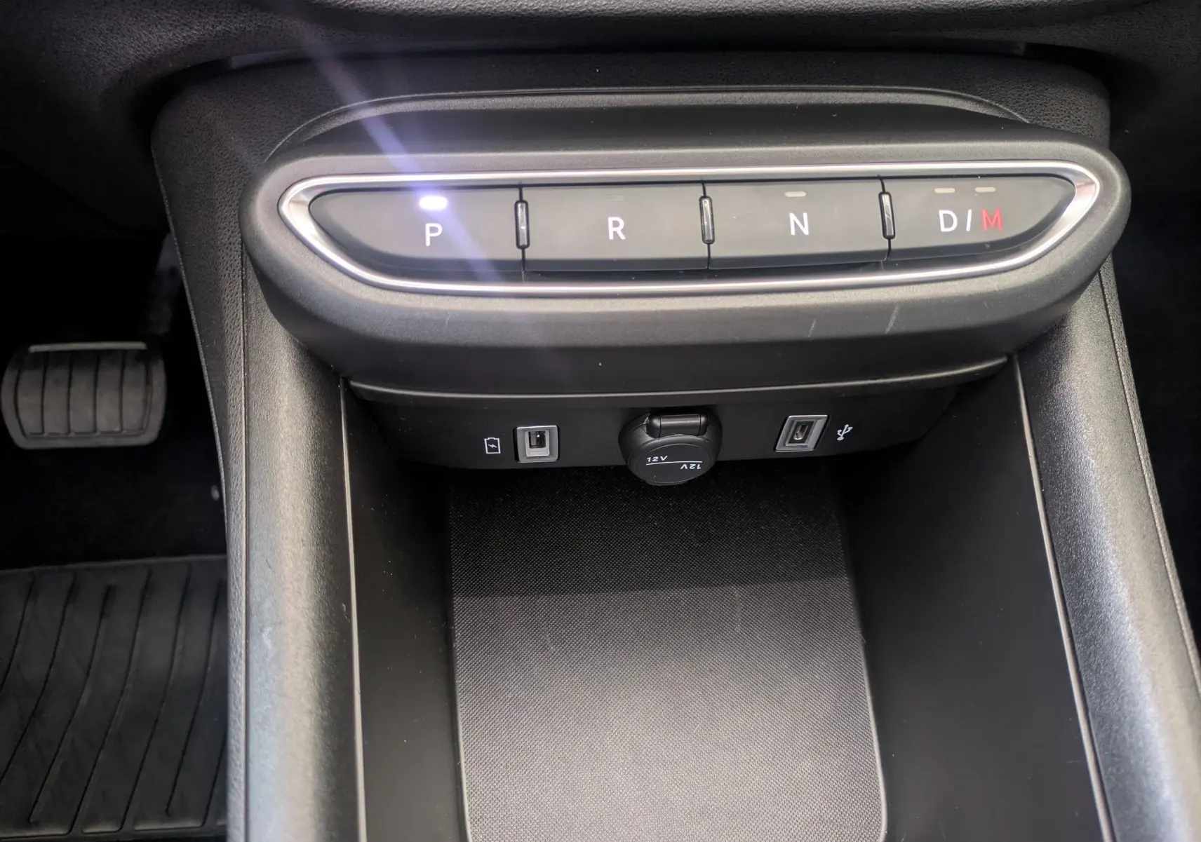 Vue rapprochée de la console centrale noire du Fiat 600 1.2 Hybrid 2025 avec boutons de boîte auto et prises USB visibles.