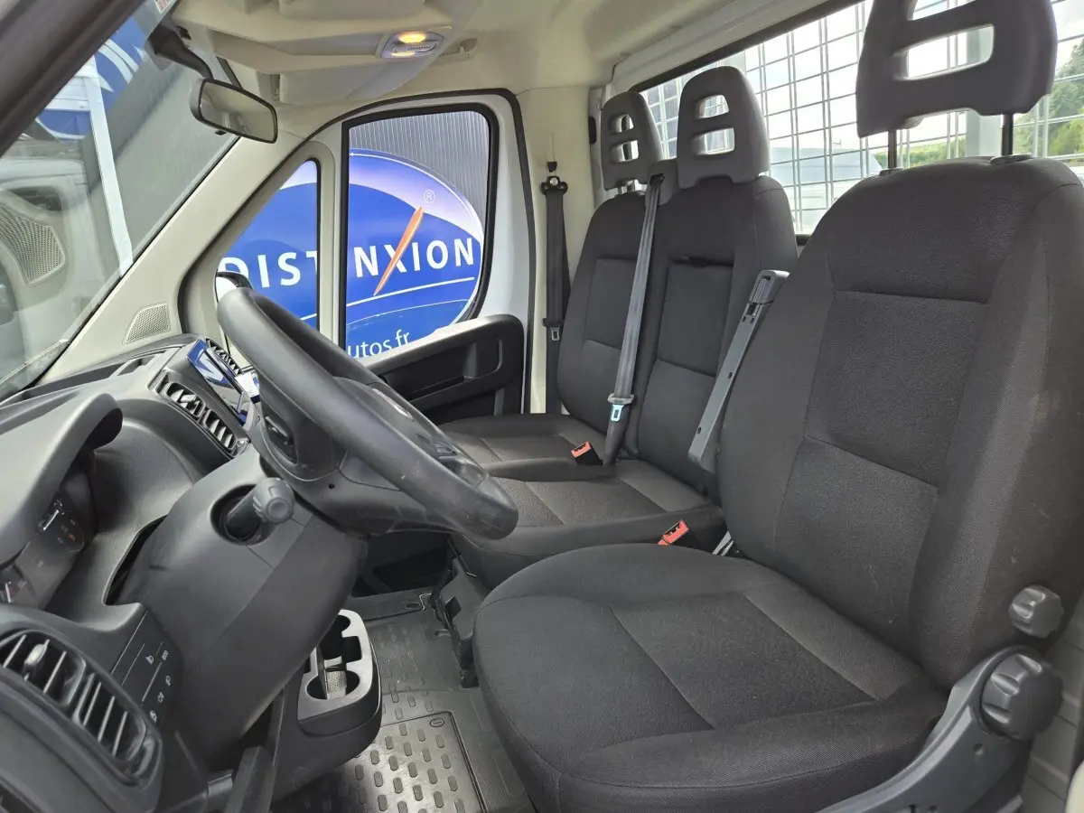 Vue intérieure côté conducteur du Fiat Ducato Fourgon blanc 2022, montrant les sièges noirs et le volant réglable.