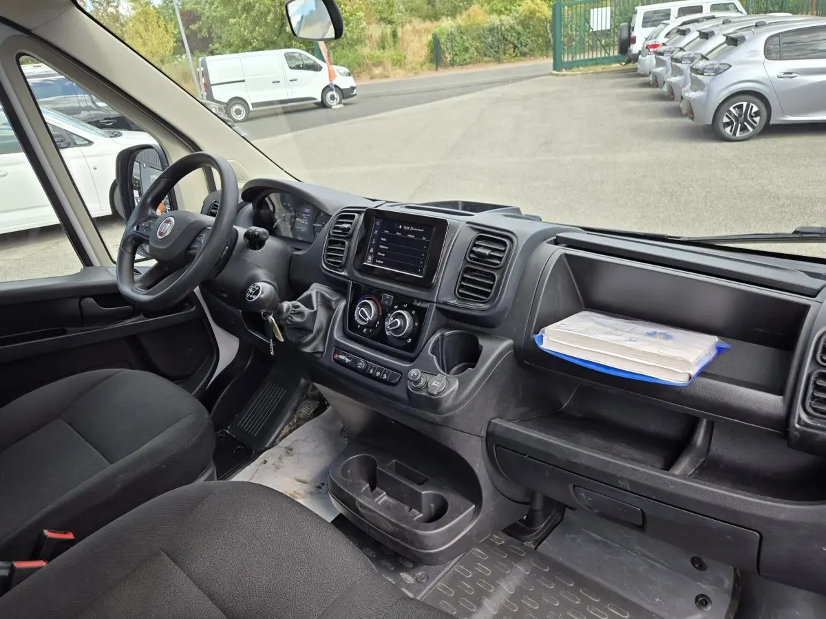 Vue intérieure côté conducteur du Fiat Ducato Fourgon blanc, montrant le tableau de bord avec écran tactile et volant noir.