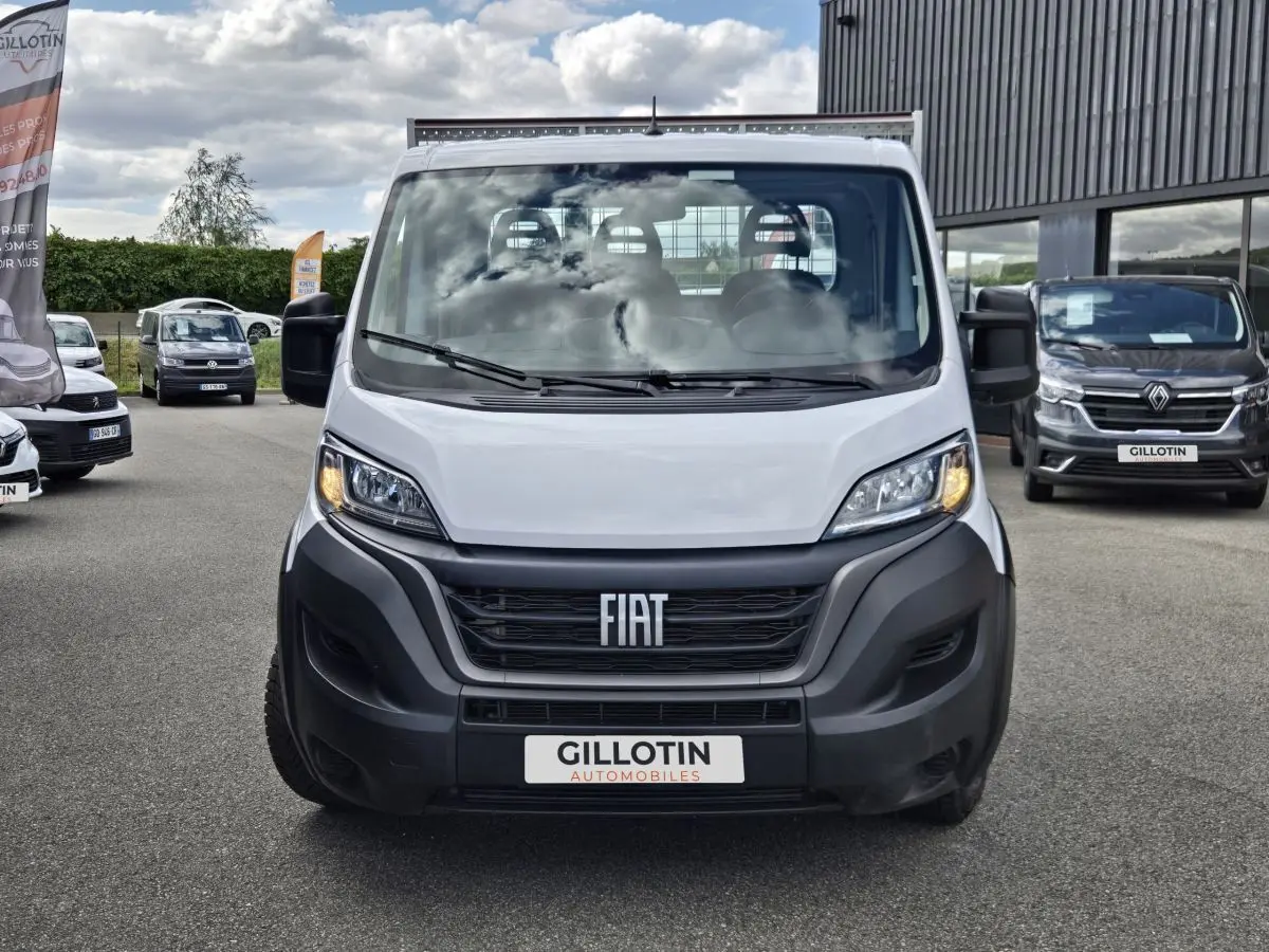 Vue frontale d’un FIAT Ducato Fourgon blanc 2022 avec calandre noire et phares allumés sur un parking extérieur.