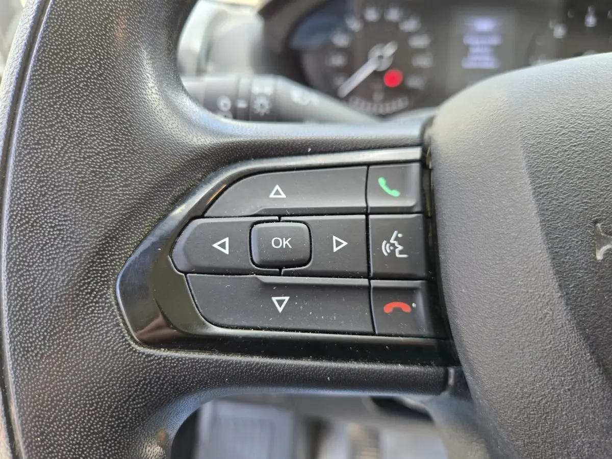 Gros plan sur les commandes gauche du volant noir du Fiat Ducato Fourgon blanc 2022, avec boutons multifonctions.