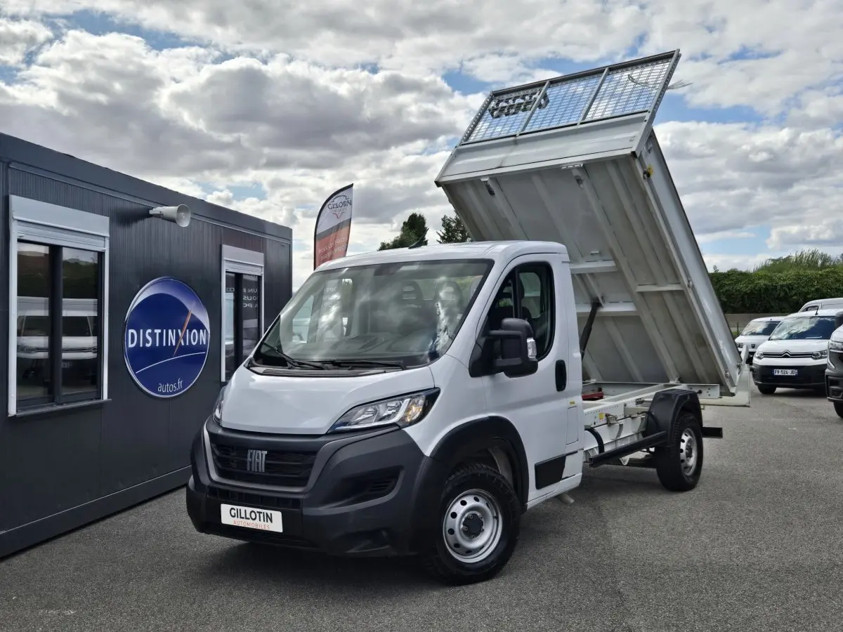 Fiat Ducato Fourgon blanc vu en 3/4 avant droit avec benne arrière relevée sur un parking extérieur.