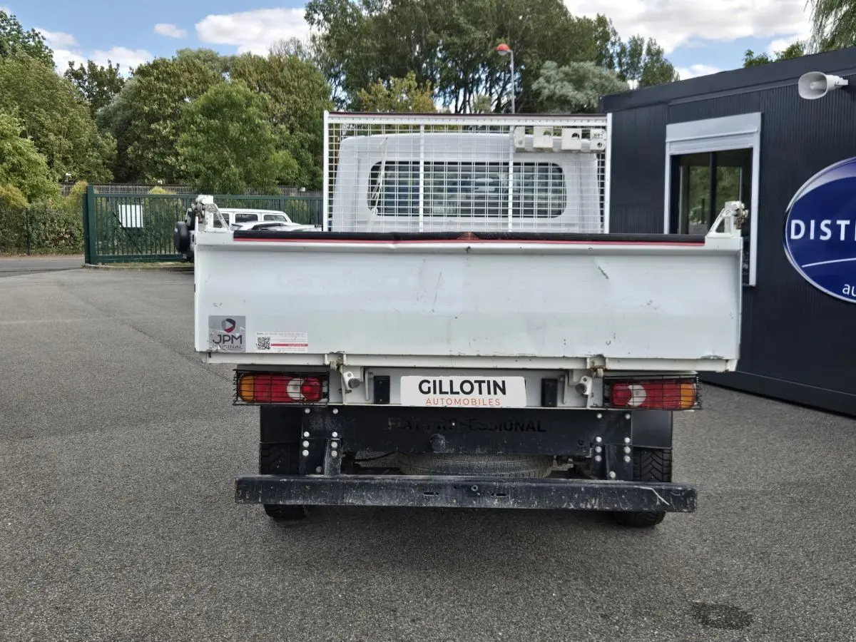 Vue arrière d’un FIAT Ducato Fourgon blanc avec benne basculante et grille de protection, stationné en extérieur.