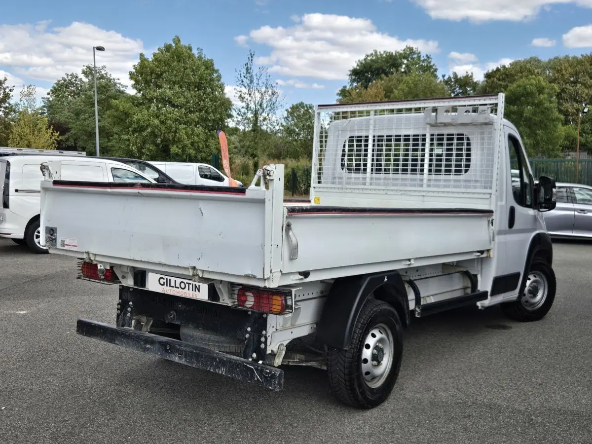 Fiat Ducato Fourgon blanc vu en 3/4 arrière droit, benne basculante avec grille de protection cabine.