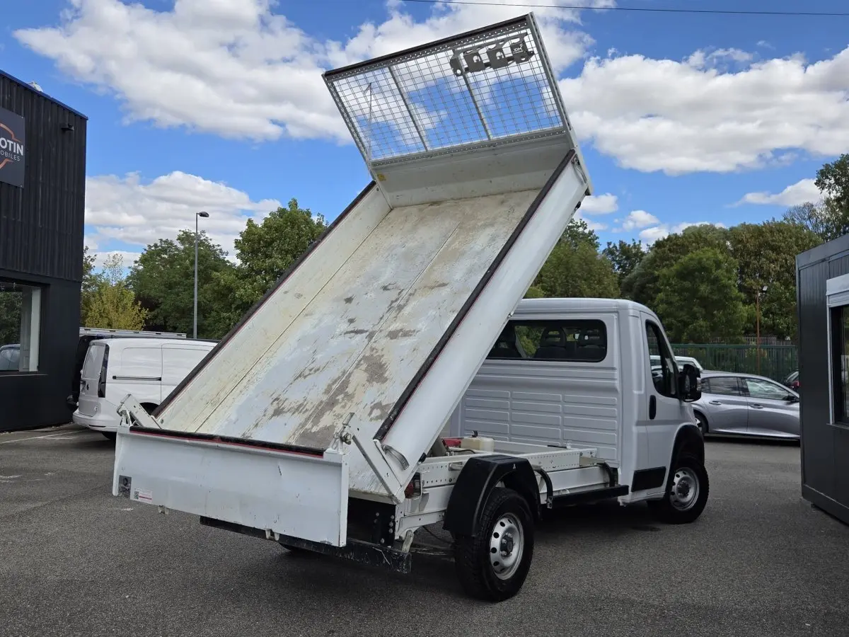 Fiat Ducato Fourgon blanc vu en 3/4 arrière avec benne basculante relevée sur parking extérieur.