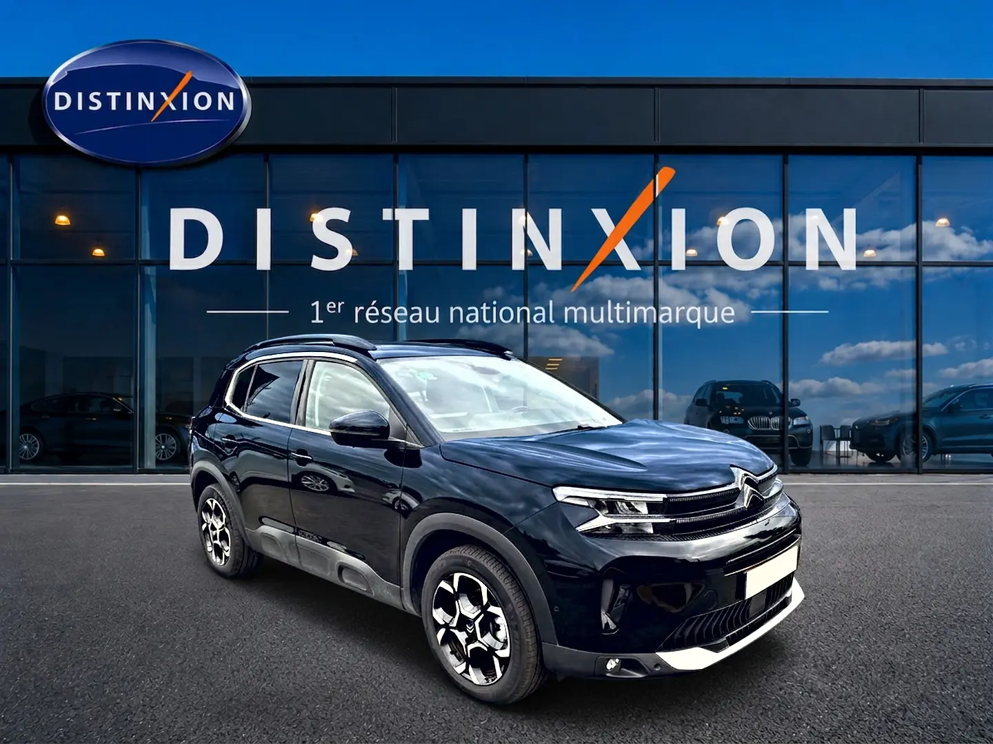 Citroën C5 Aircross noir en 3/4 avant droit, avec jantes alu et barres de toit visibles devant une vitrine Distinxion.
