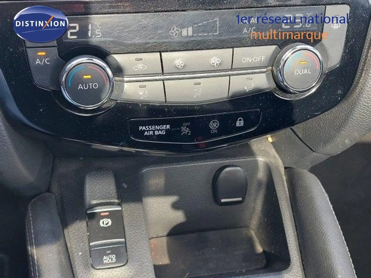 Gros plan sur la console centrale du Nissan Qashqai blanc lunaire, montrant les commandes de climatisation et frein à main électrique.